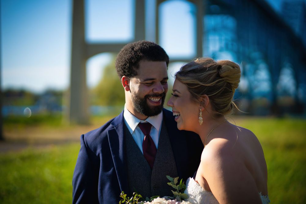 A couple shares an intimate moment on their wedding day in a sun-lit outdoor setting with green grass and soft bokeh.