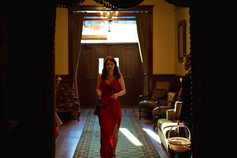 A silhouette in a red dress stands in a sunlit doorway of an elegant room.