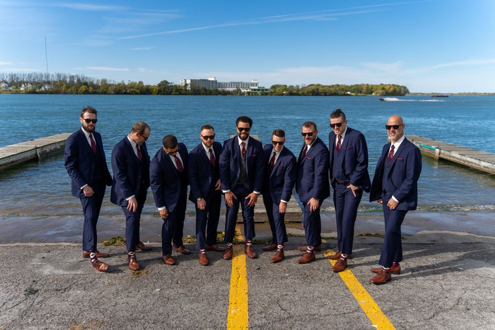 Groomsmen in navy suits pose on dock with waterfront skyline backdrop.