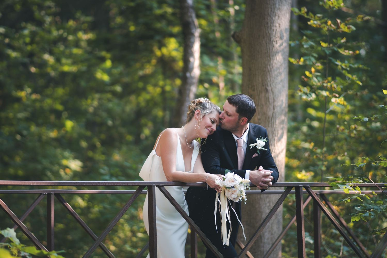 A couple shares an intimate moment on a wooden bridge surrounded by trees.