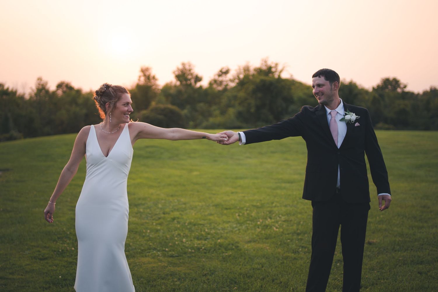 A couple dances together on a grassy lawn at sunset in their wedding attire.
