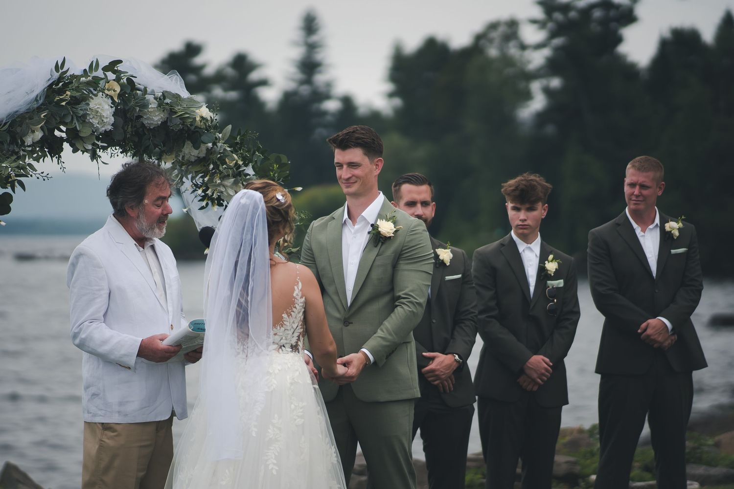 Seaside wedding ceremony with participants gathered under a decorated arch.