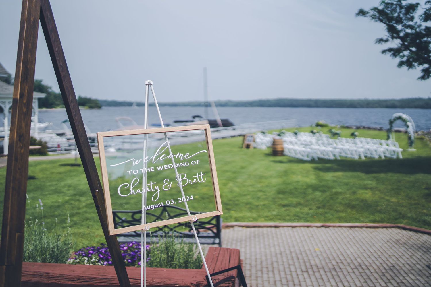 Waterfront wedding ceremony setup with clear acrylic welcome sign and lake view.
