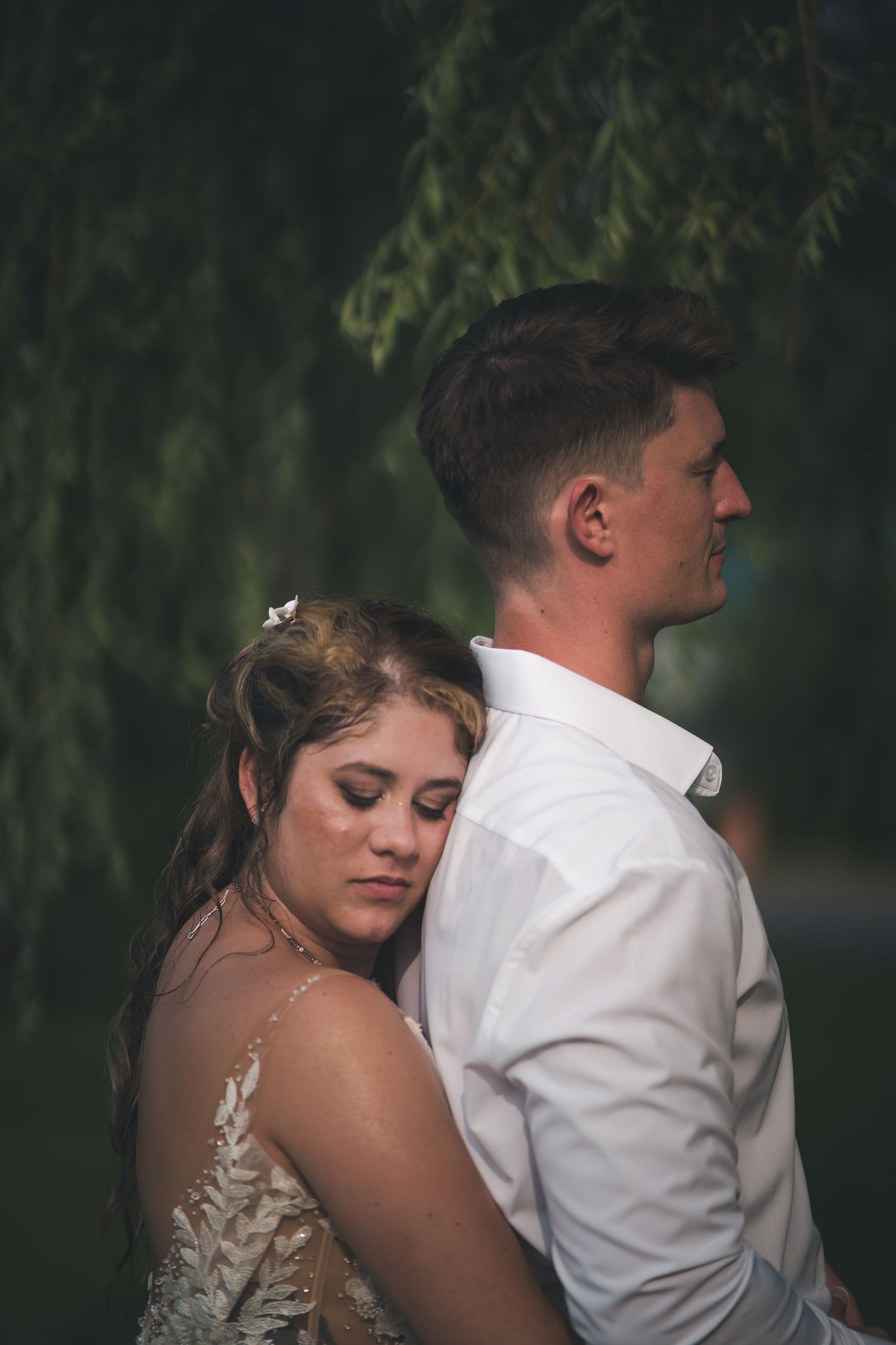 Intimate portrait of newlyweds embracing under willow trees.