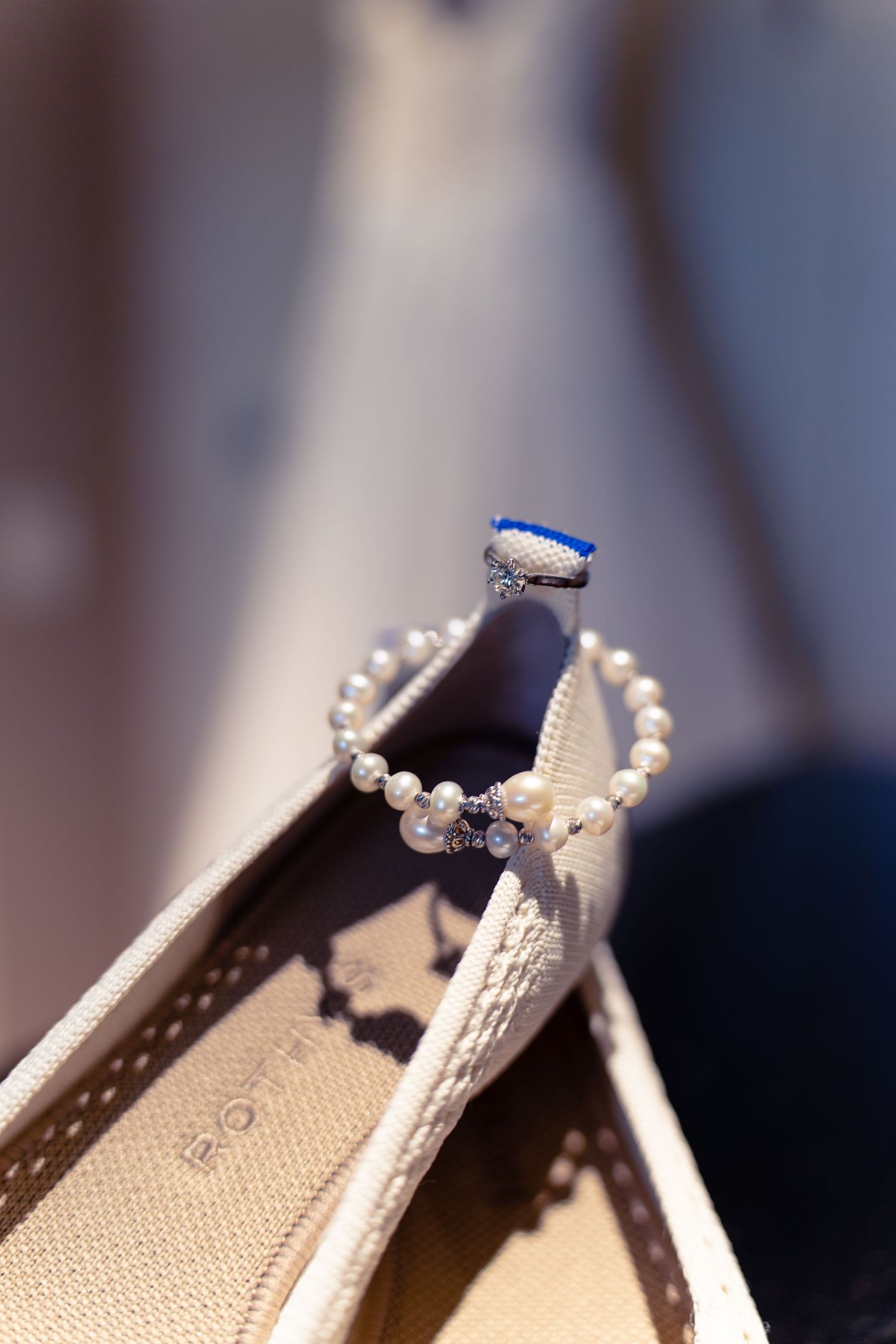 A delicate pearl bracelet rests on the edge of an elegant beige wedding shoe.
