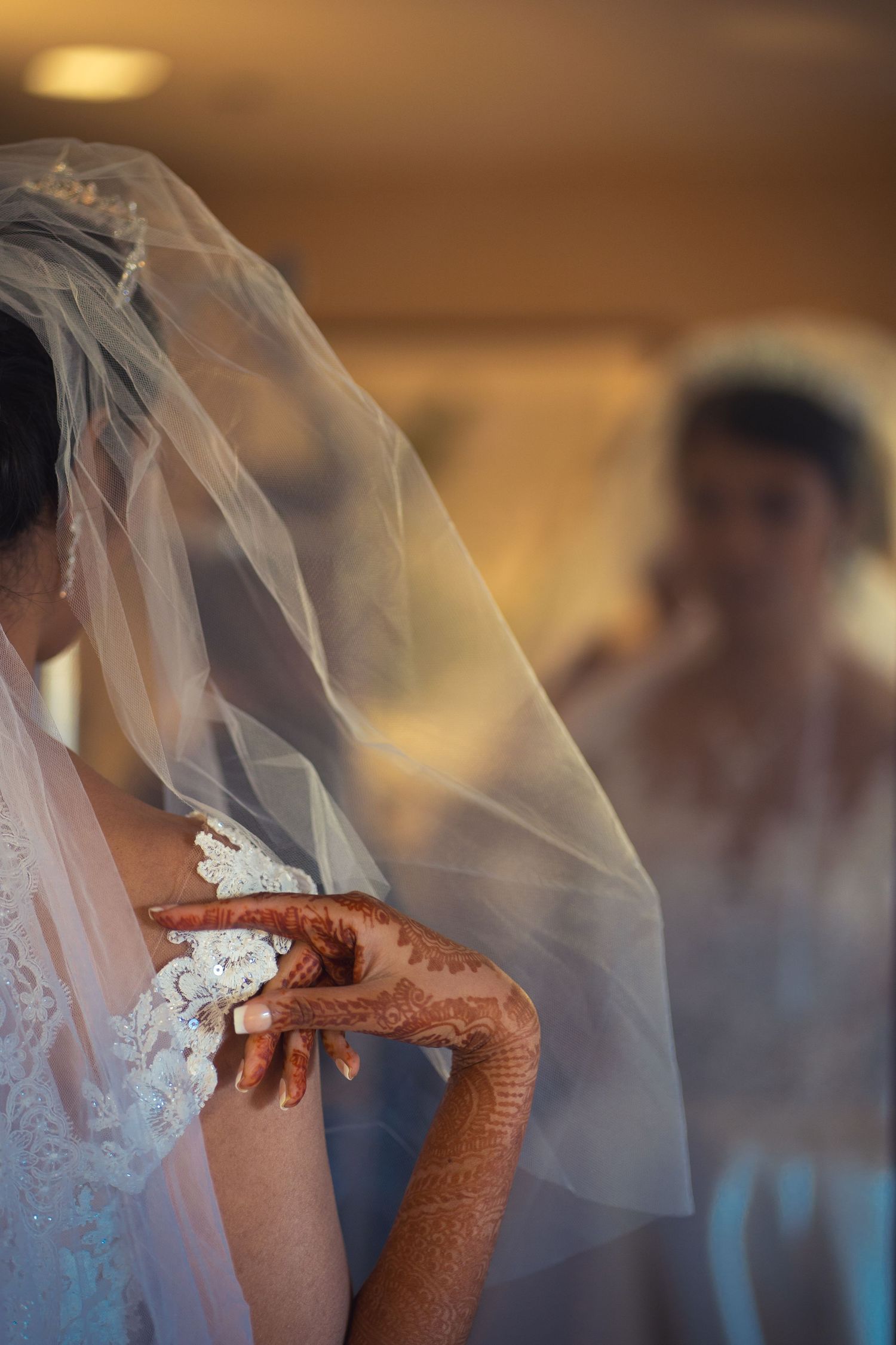 Intricate henna designs decorate hands beneath a flowing white bridal veil.