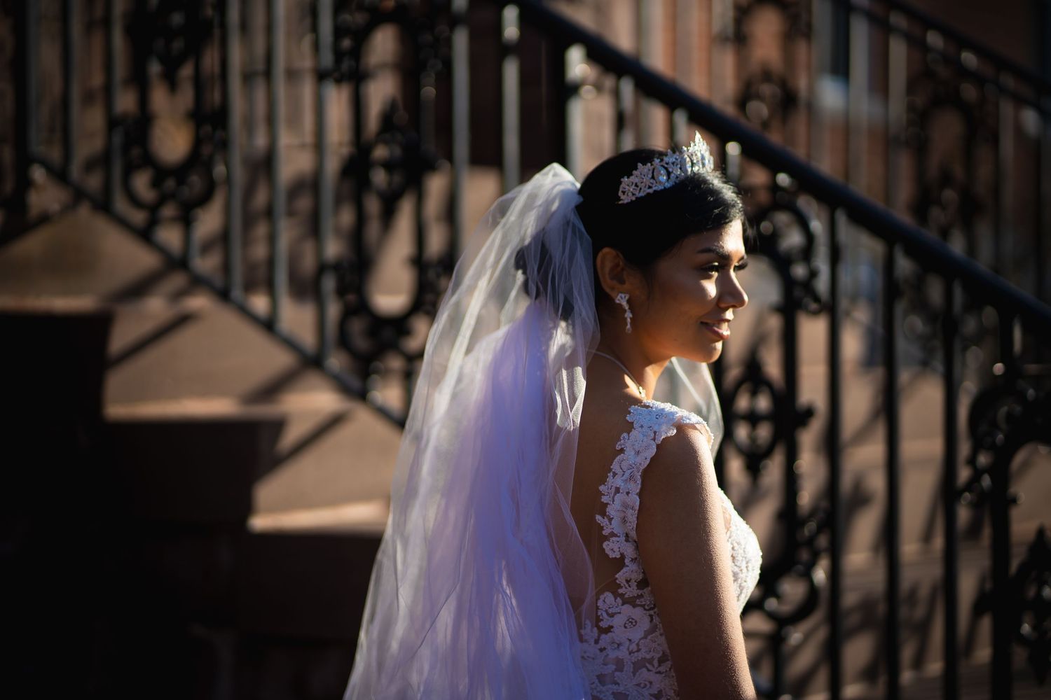 A white wedding dress and veil flow against an ornate iron staircase backdrop.