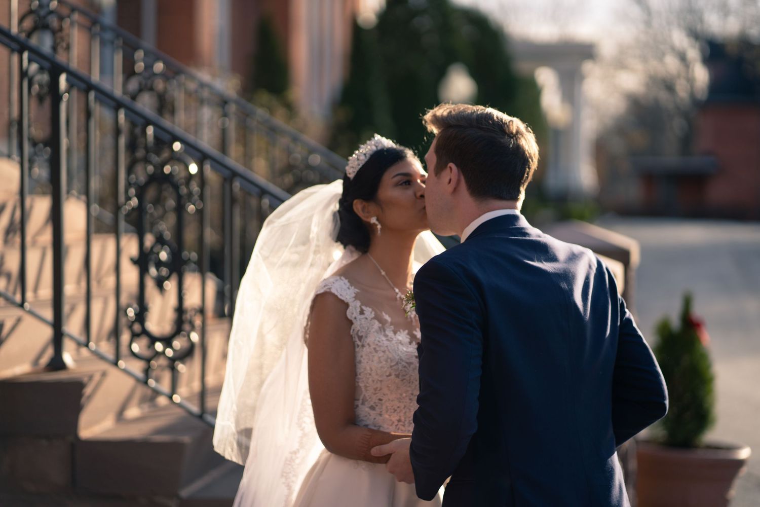 A romantic wedding kiss captured against ornate iron stairs.