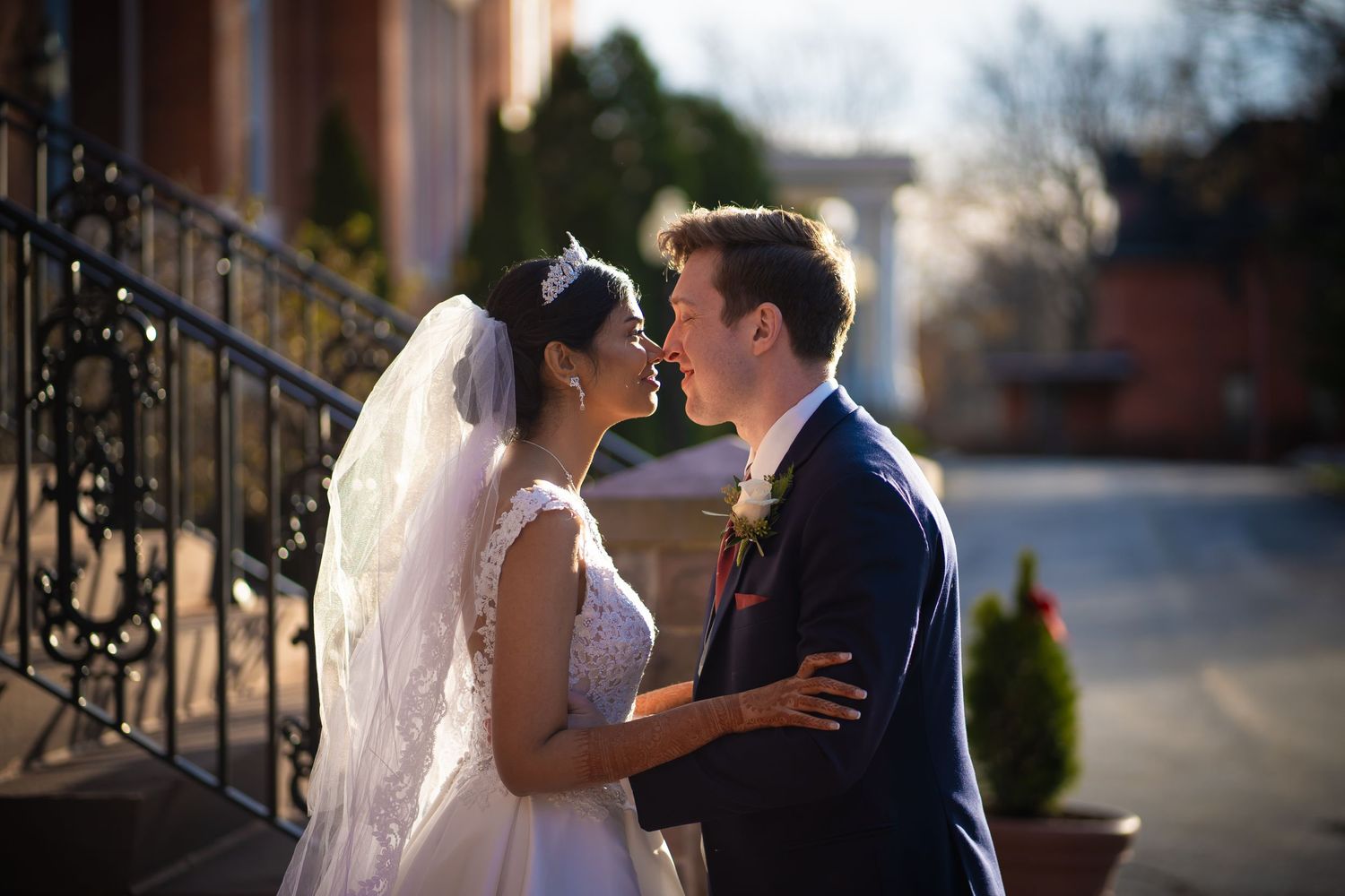 A romantic wedding photo of a couple embracing outside a brick building in warm evening light.