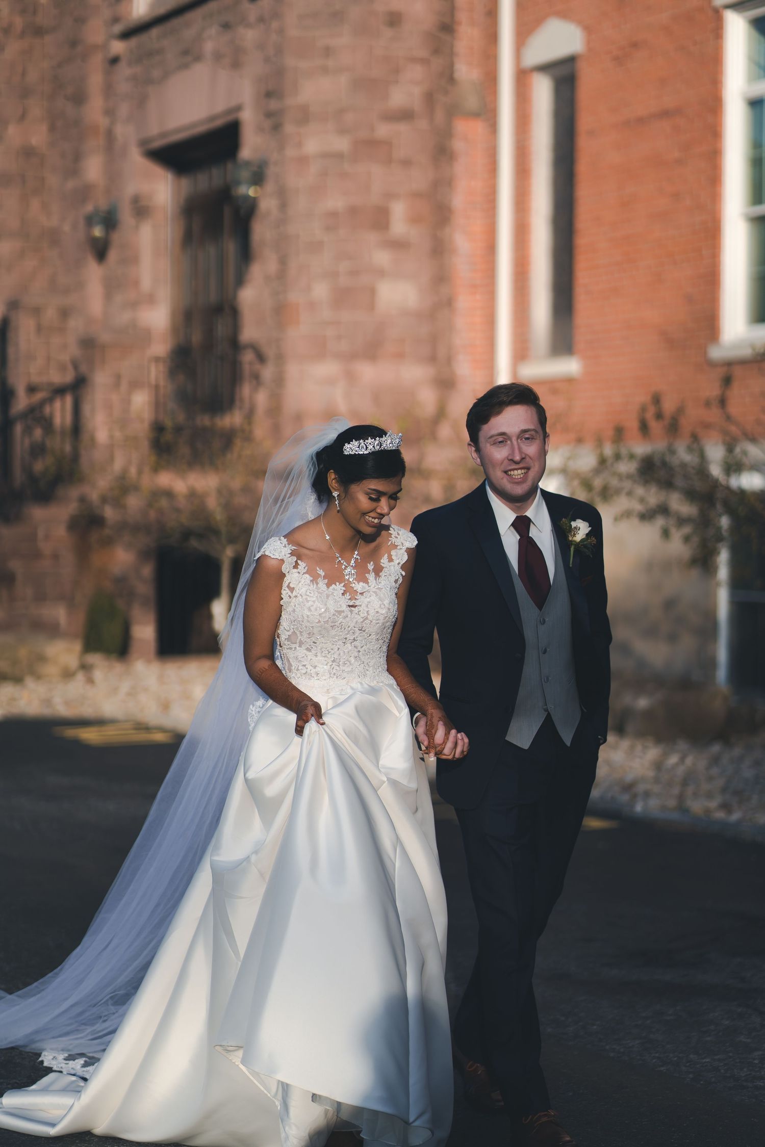 A bride and groom pose together outdoors against a historic brick building backdrop.