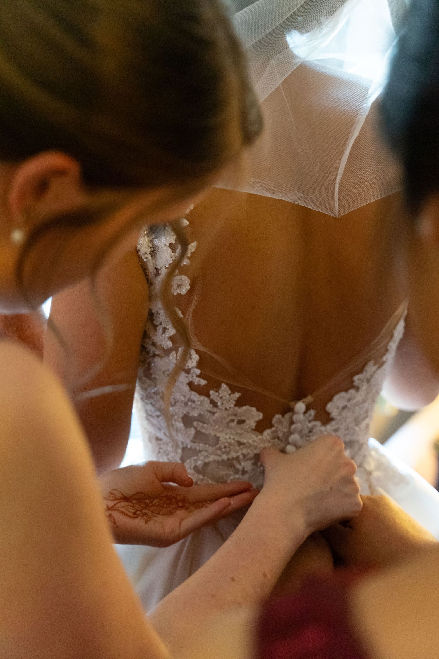 Close-up detail of intricate lace on a white wedding dress being fastened.