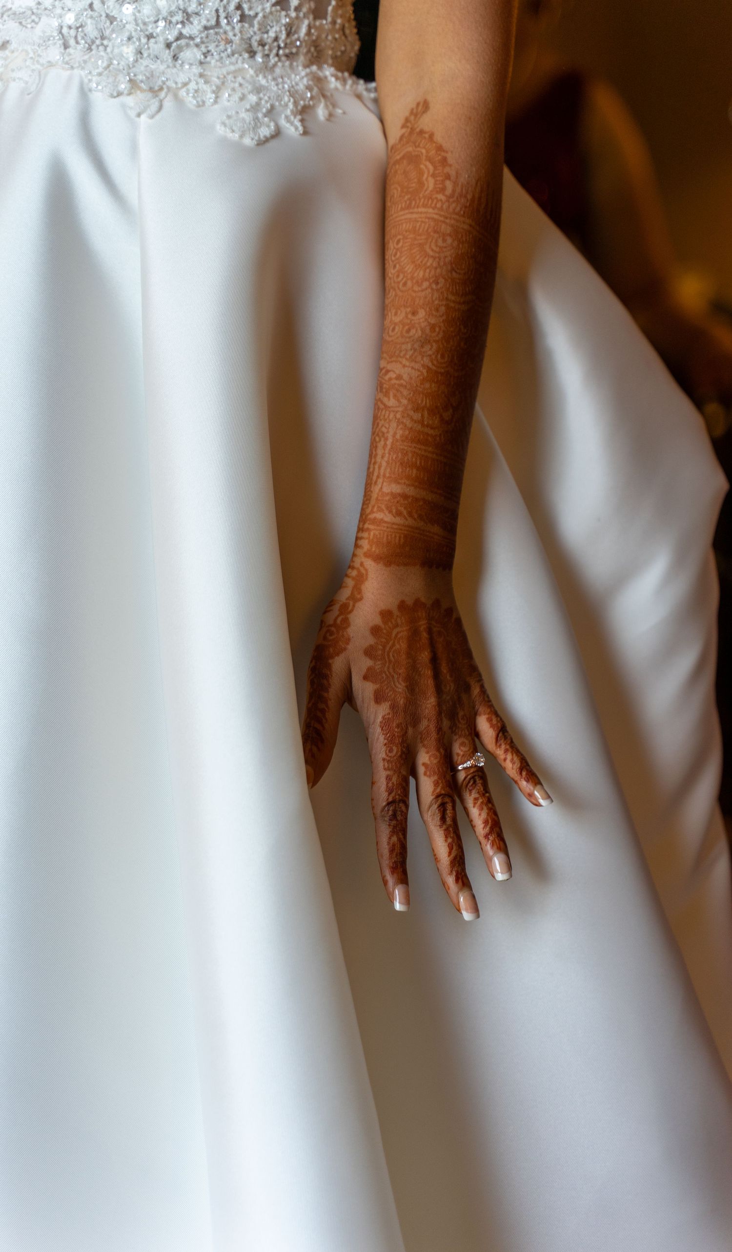 Detailed henna design adorns a hand against white wedding dress fabric.