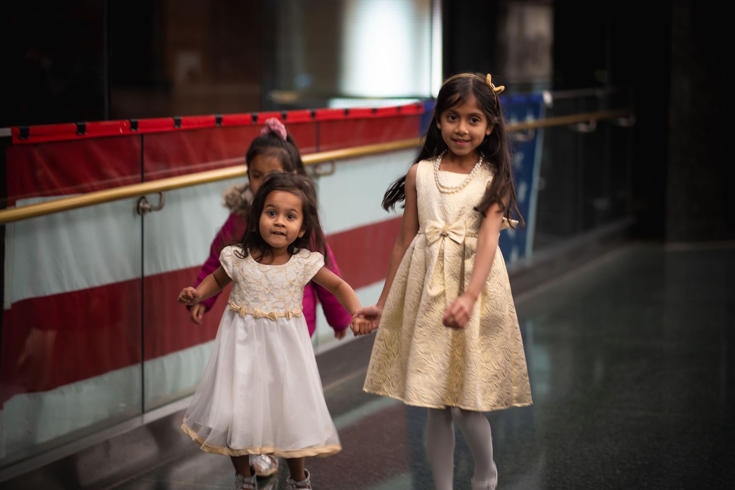 Two young girls in pretty dresses walking together in a hallway.
