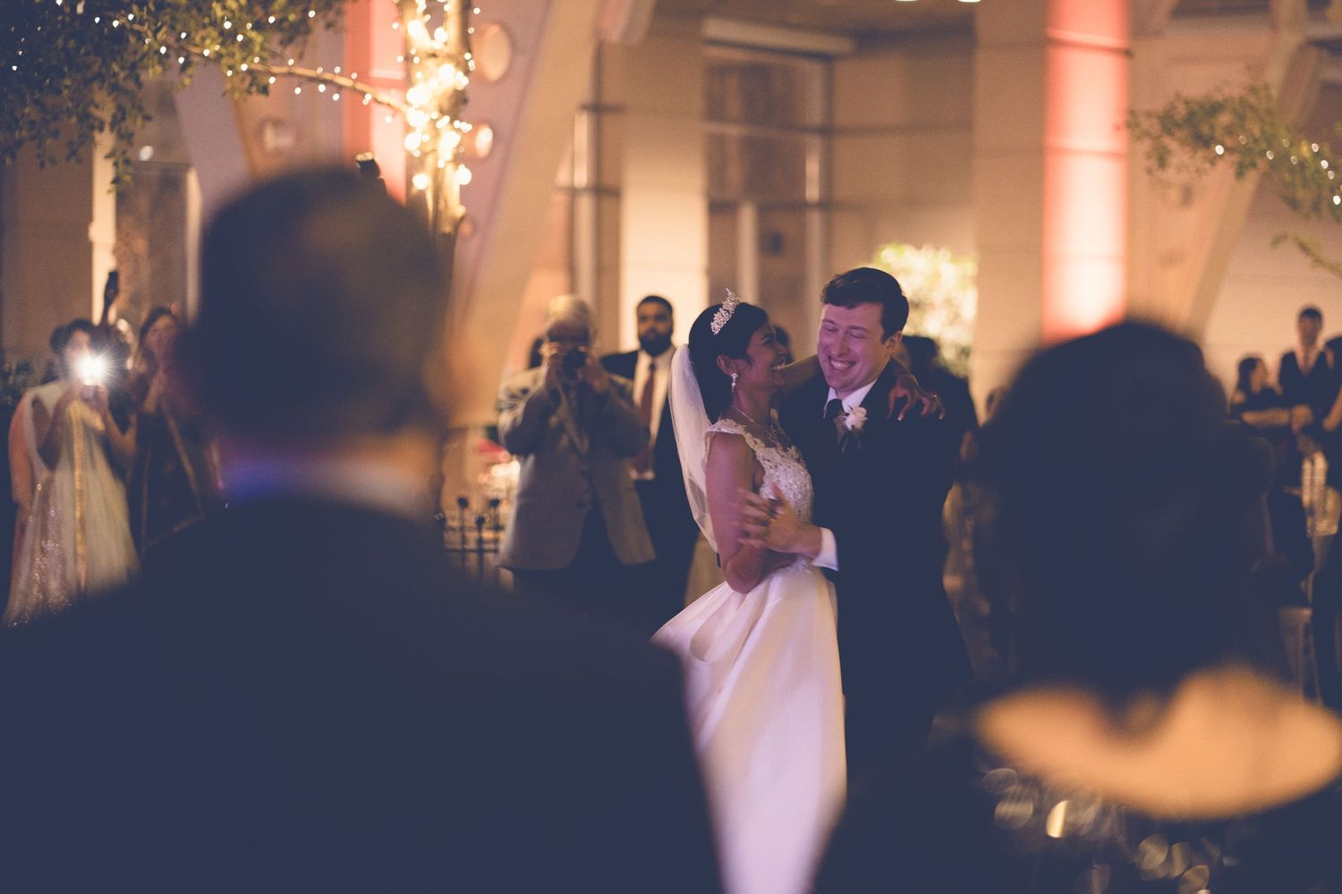 Couple sharing their first dance surrounded by guests at a dimly lit wedding reception.