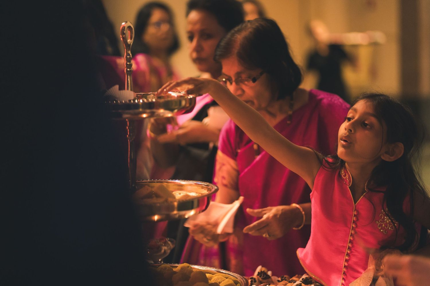 Wedding guests serving food from a buffet table in warm ambient lighting.
