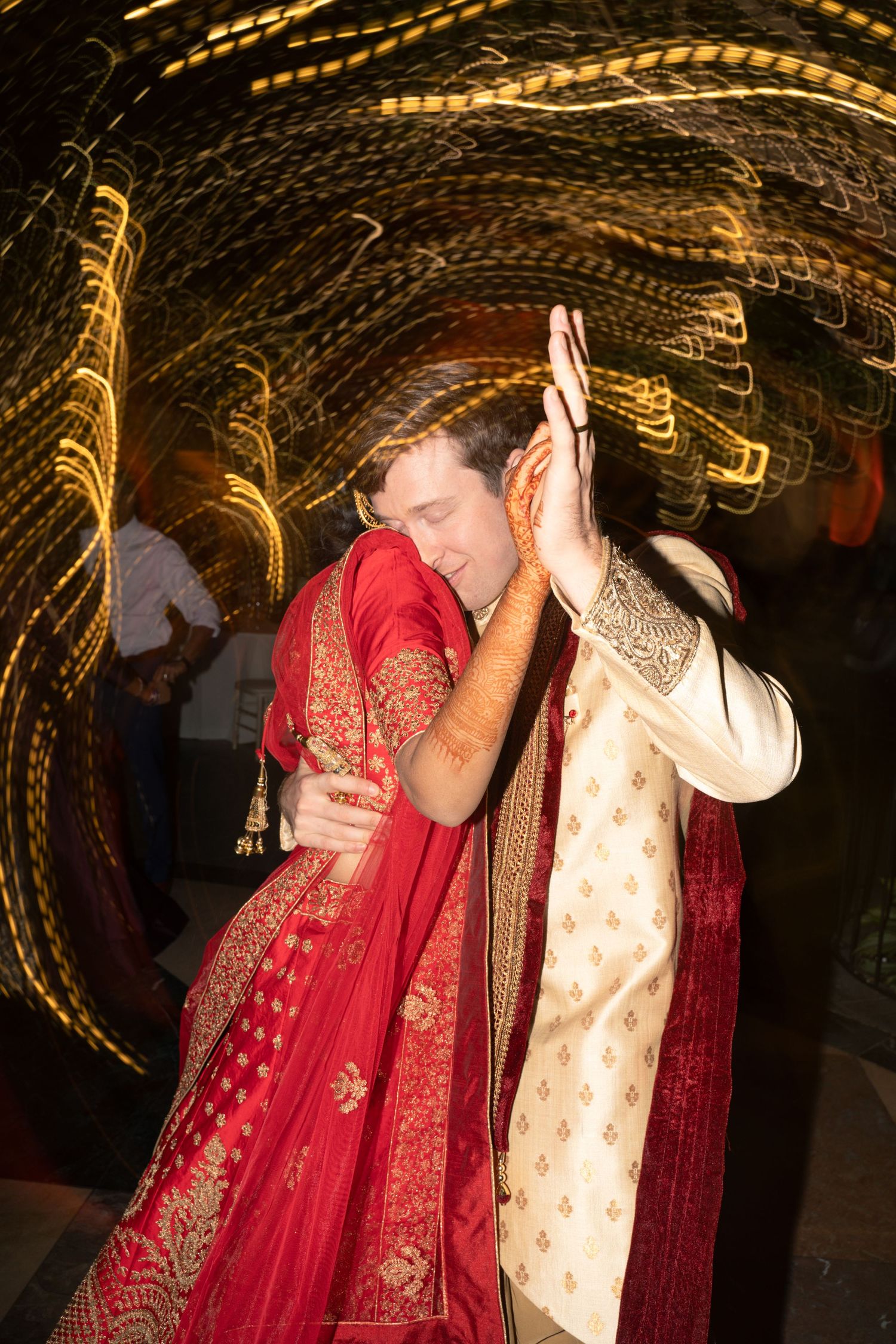 Couple in traditional Indian wedding attire sharing an intimate dance moment with swirling lights.
