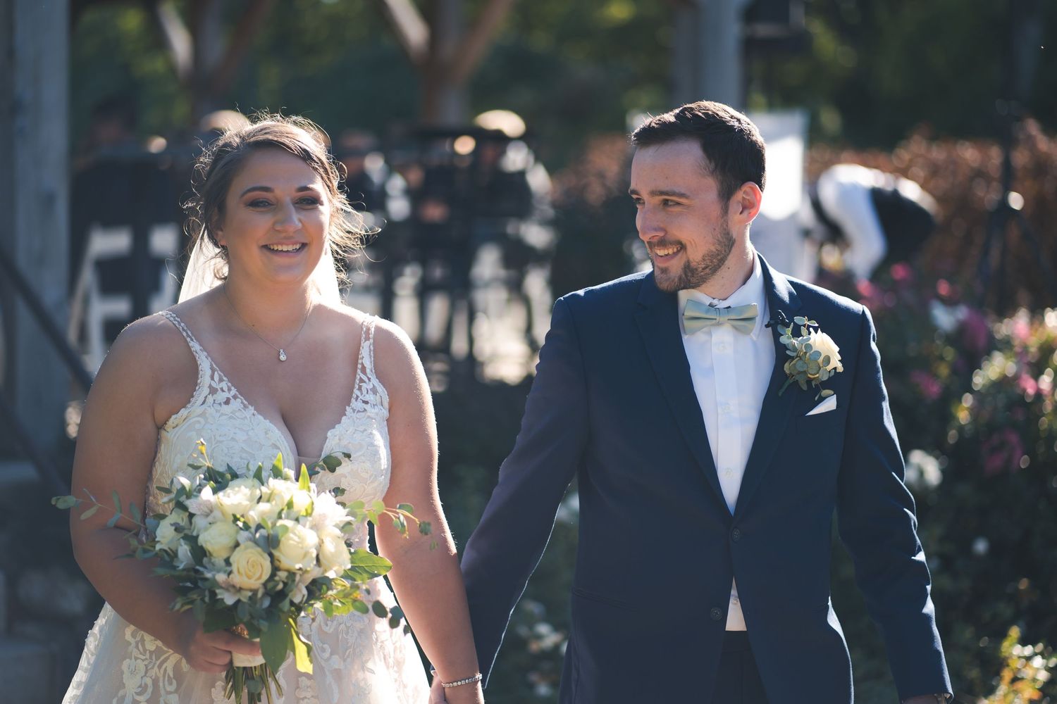 A joyful couple walks together after their ceremony with a beautiful yellow and white bouquet.