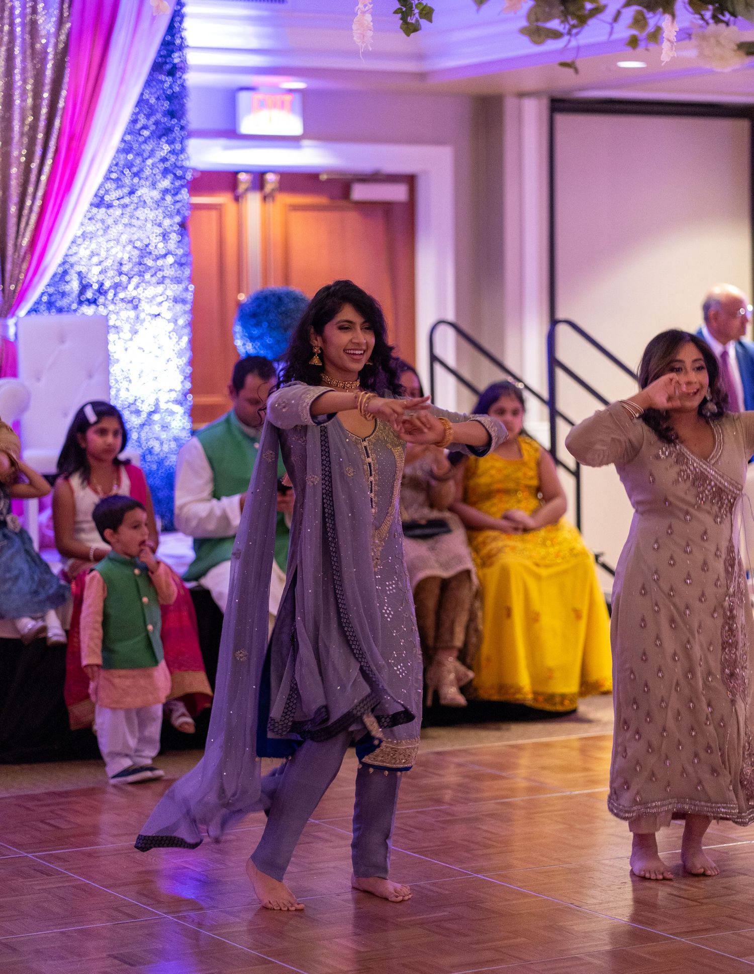 Traditional Indian dance performance at a wedding reception with purple and pink stage lighting.
