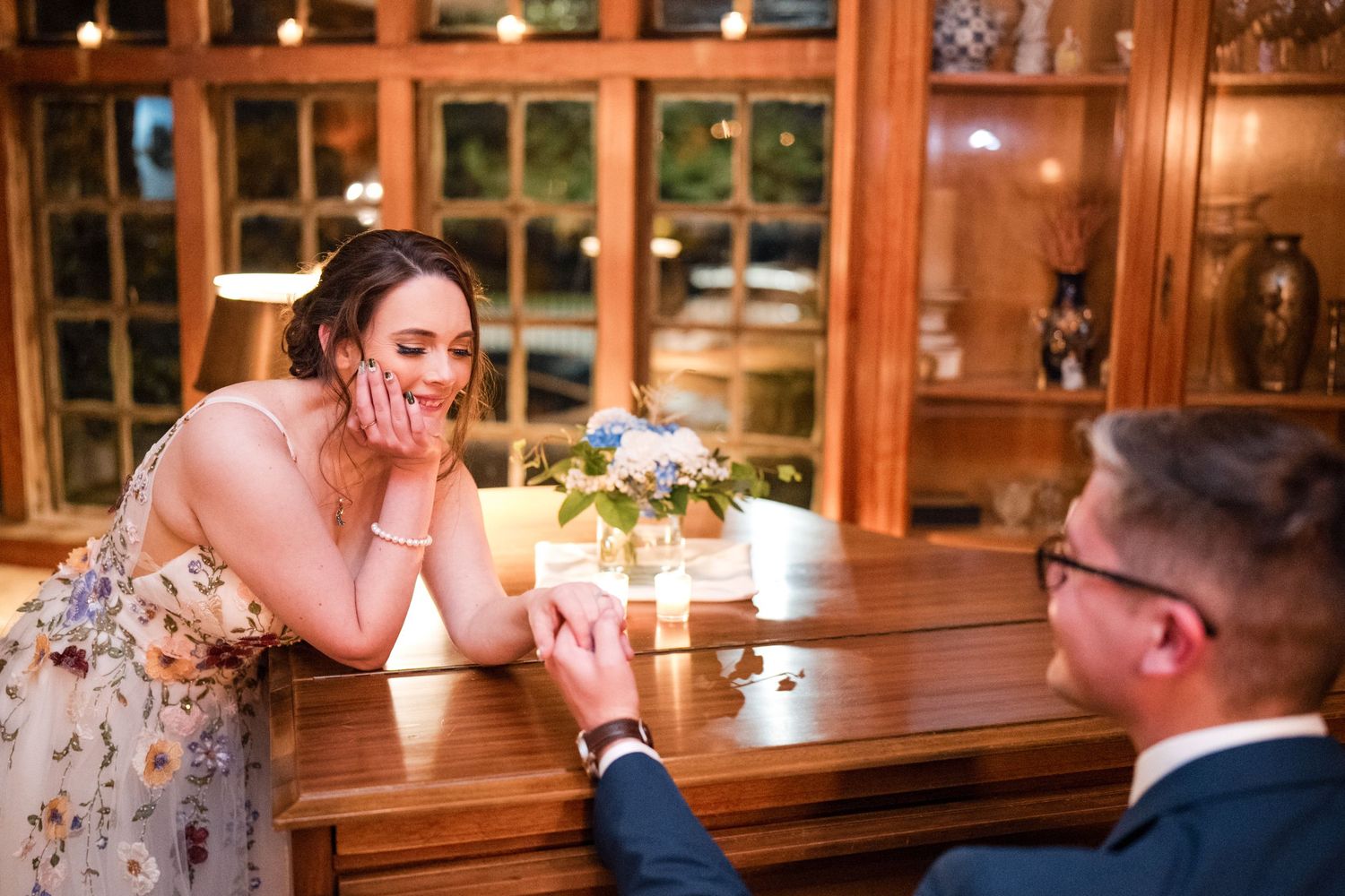 A romantic candlelit proposal scene at a wooden table in an intimate setting.
