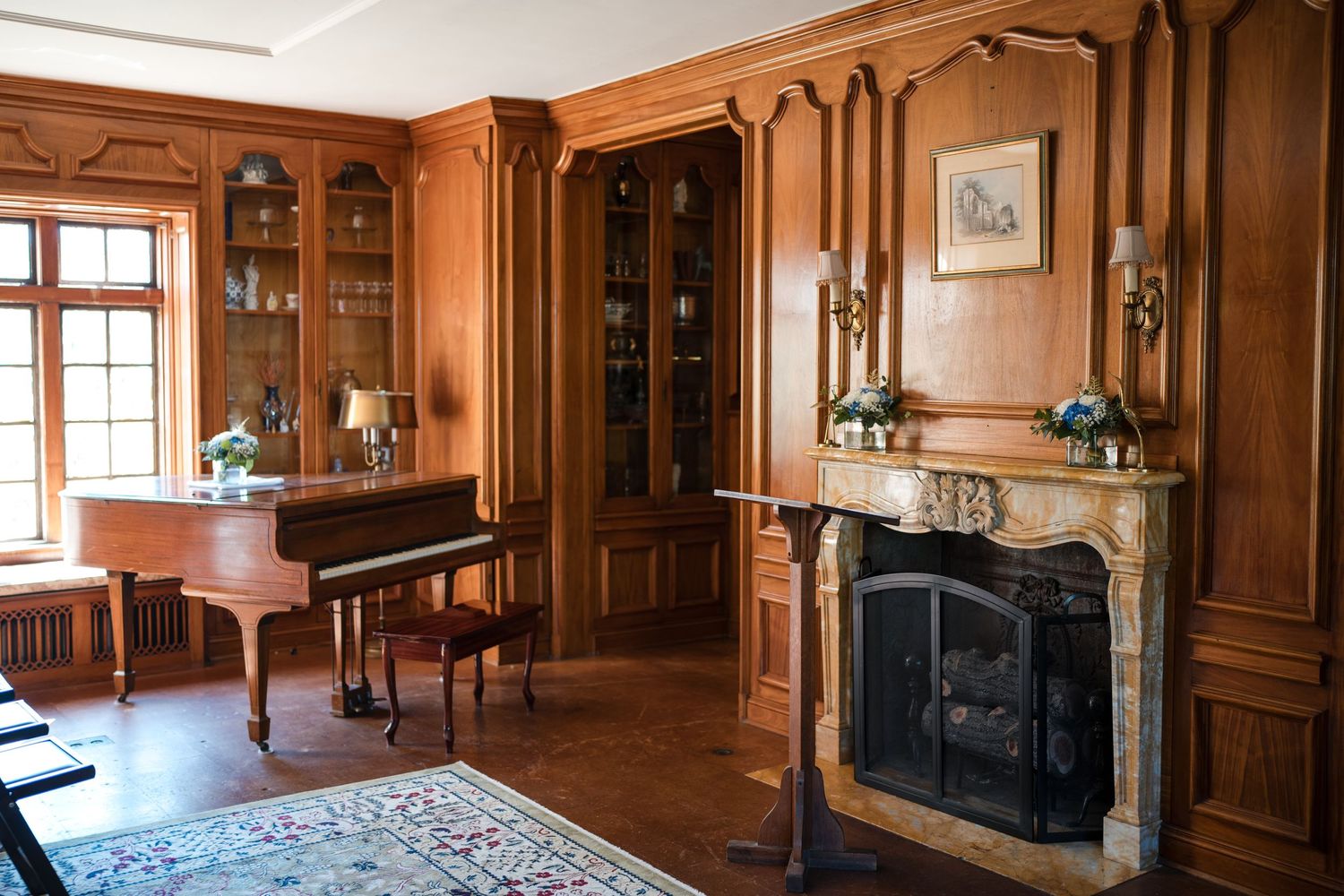 Elegant wood-paneled room with fireplace, oriental rug and grand piano.