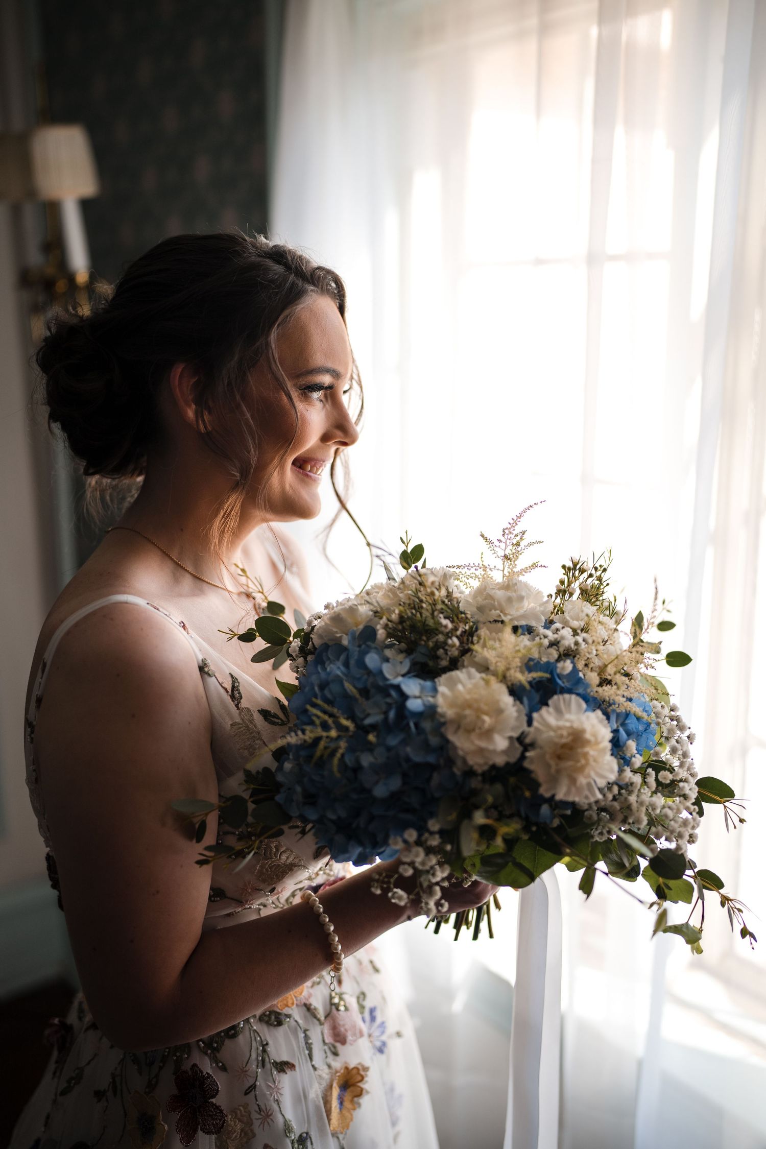 A bridal bouquet of blue and white flowers held near a sunlit window.
