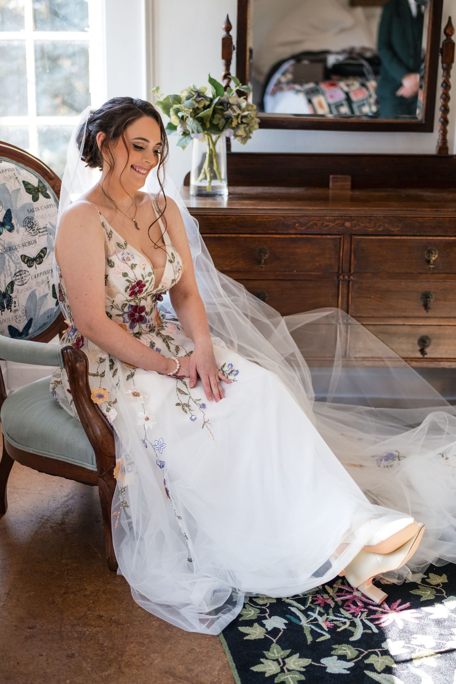 A floral wedding dress elegantly displayed on an antique chair near a wooden dresser.