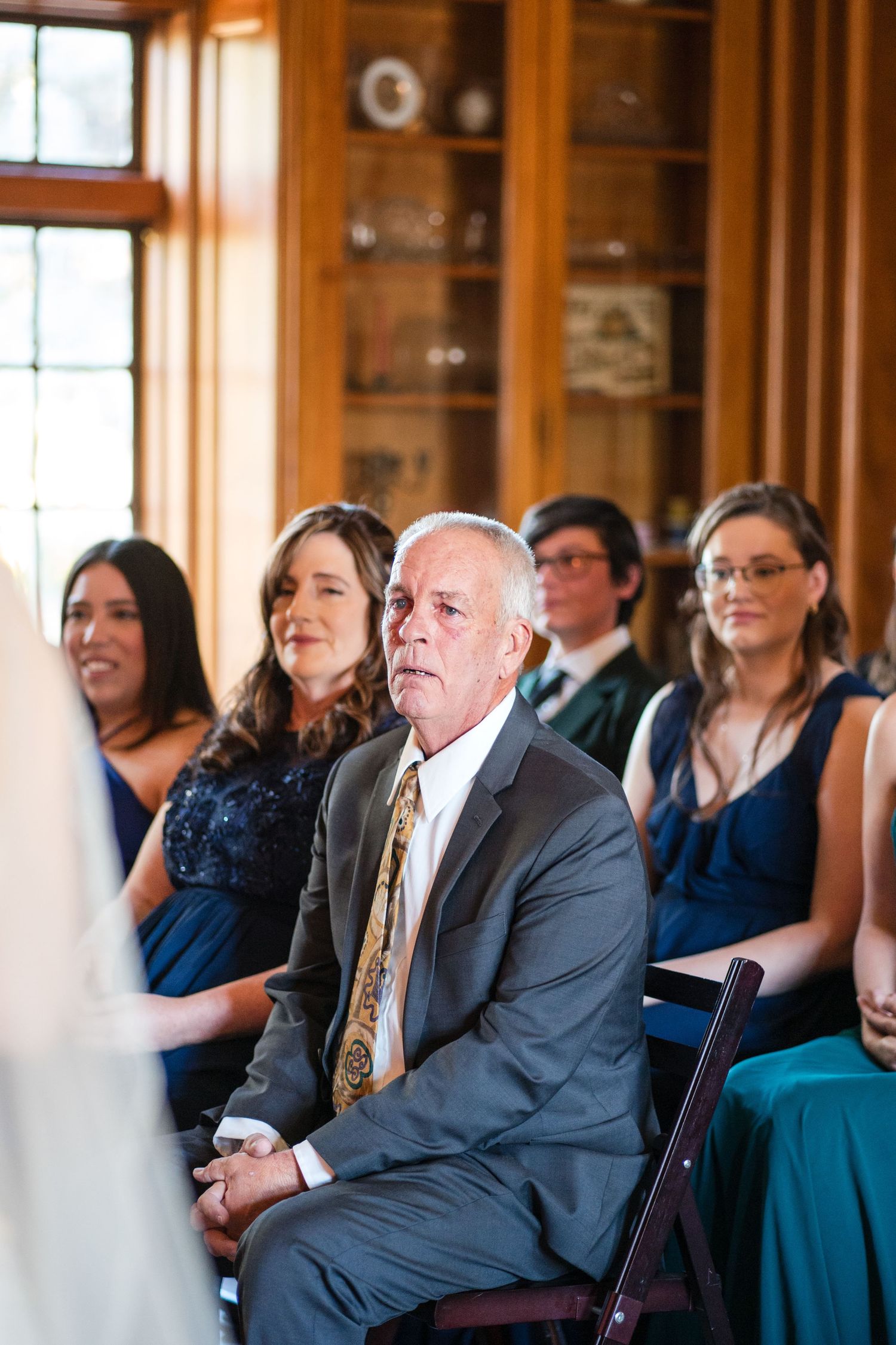 Wedding guests in formal attire seated during an indoor ceremony.