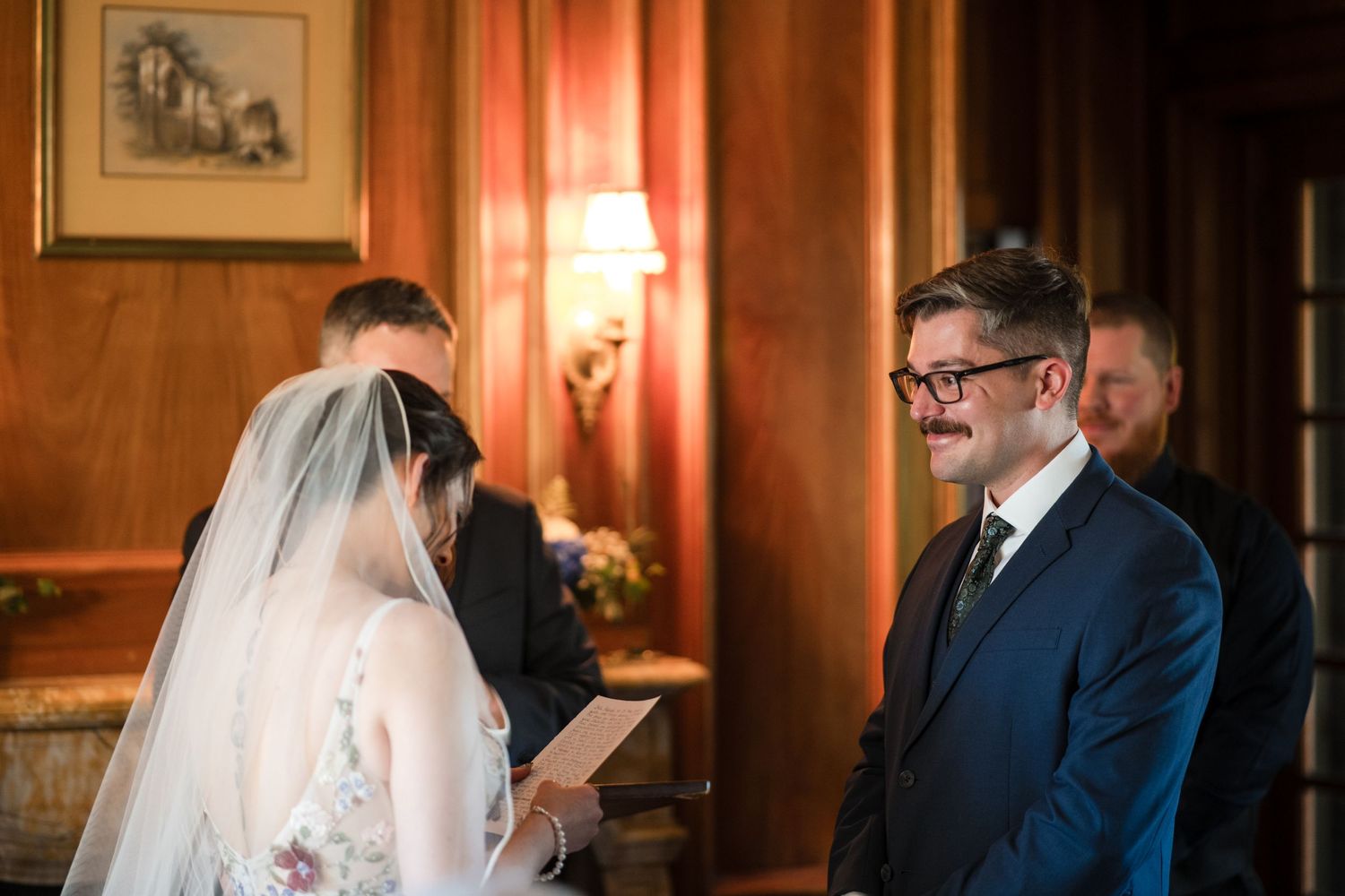 A wedding ceremony in an elegant wood-paneled room with warm lighting and wall sconces.