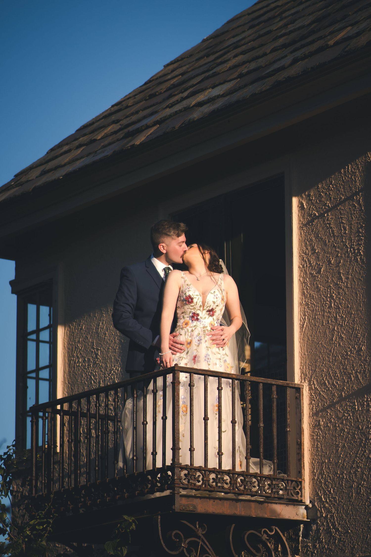 Couple embraces on a rustic balcony during golden hour wedding photography.
