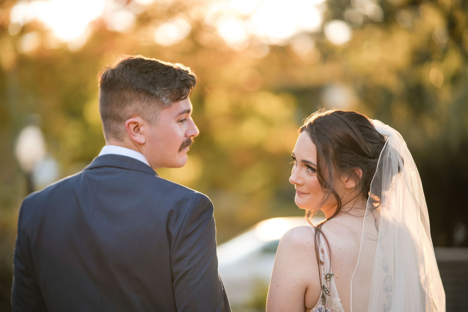 Sunset wedding portrait with bride in veil and groom in navy suit against warm lighting.