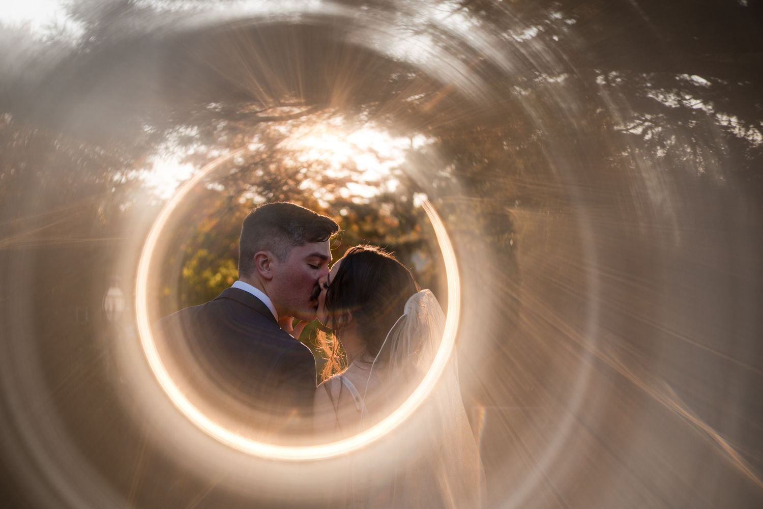 Creative wedding photography through a circular tunnel with dramatic lighting and flare effects.
