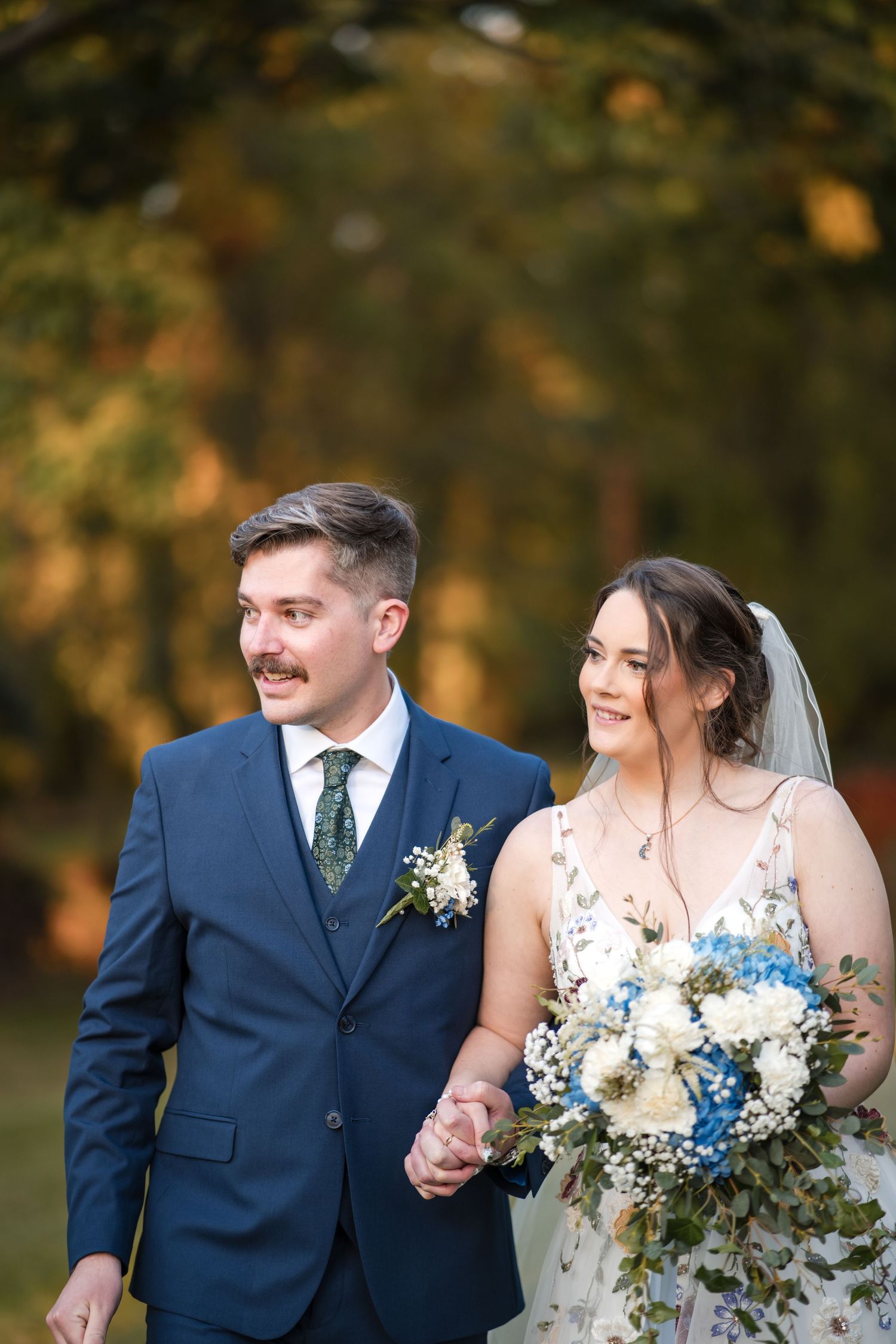 A couple on their wedding day walking together outdoors during autumn with beautiful fall foliage.