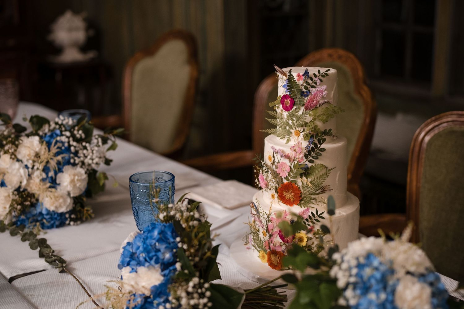 Elegant wedding cake decorated with blue and pink flowers on a formal dining table.