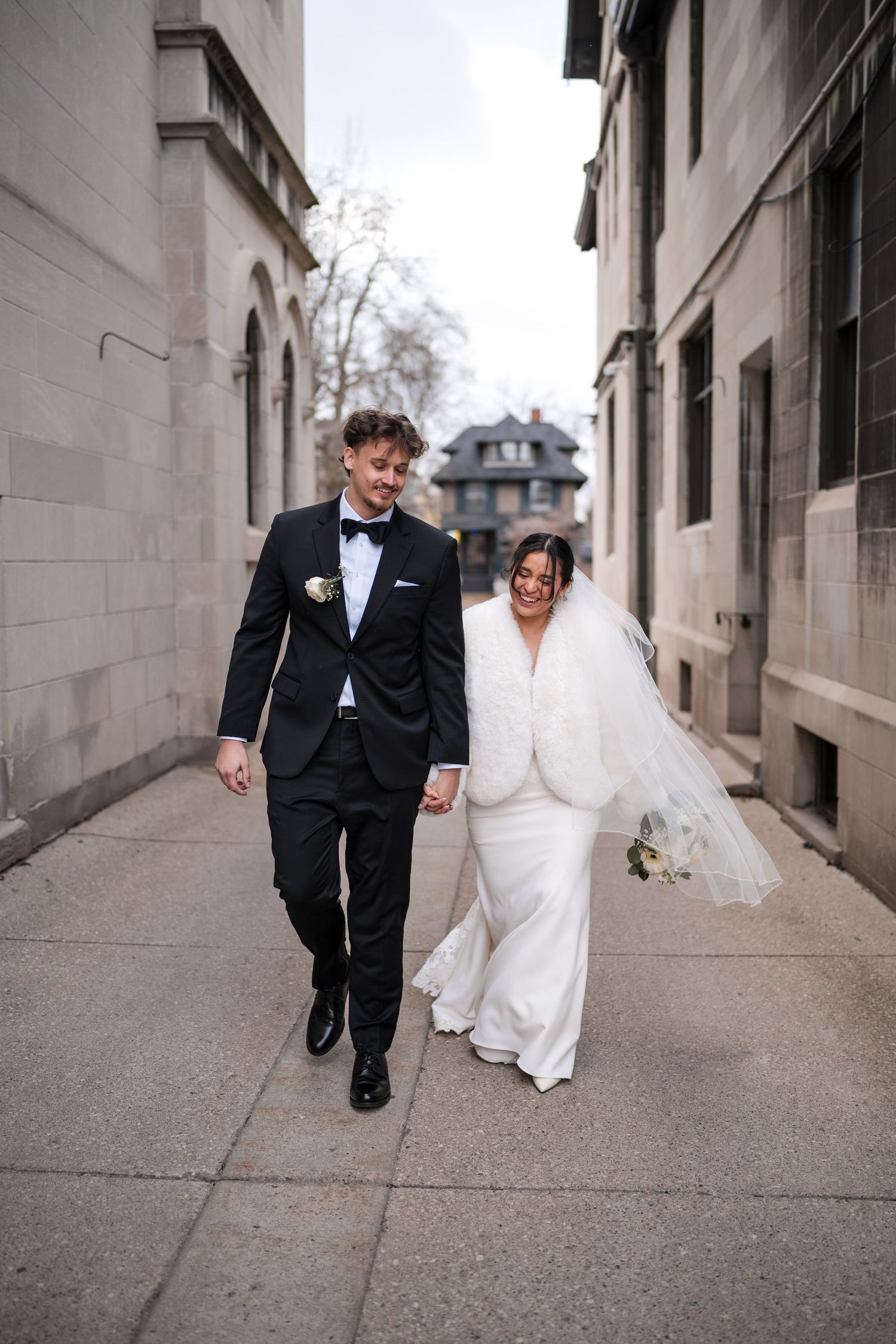 A bride and groom walking through an urban alley decorated with historic stone buildings on their wedding day.