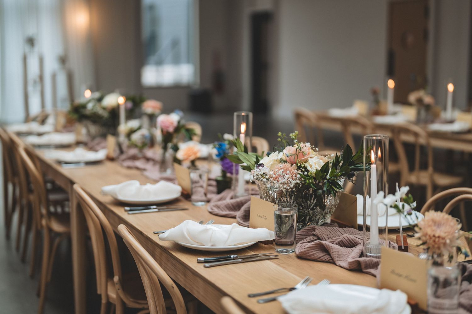 Rustic wedding reception table decorated with white floral centerpieces, kraft paper placemats and wooden chairs.