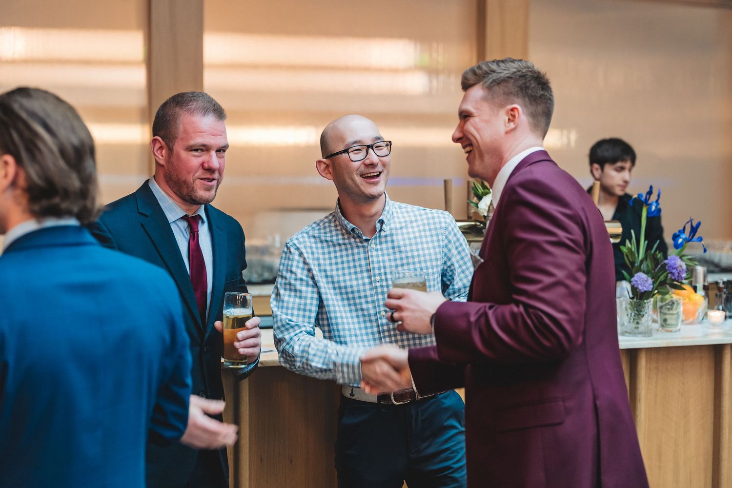 Three people engage in conversation at a social gathering while holding drinks in an office or event space.