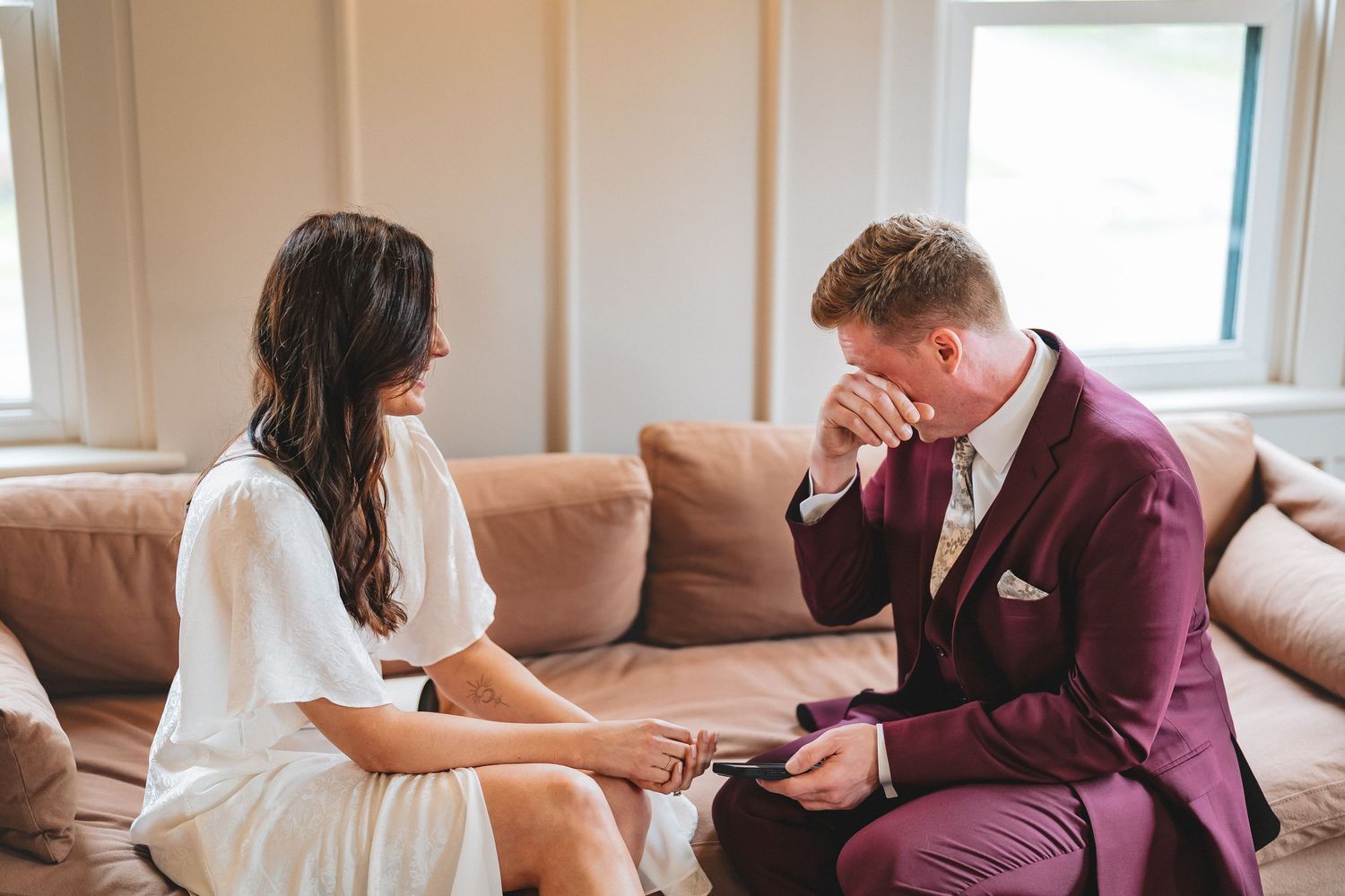 An emotional moment shared between two people in formal attire sitting on a beige couch during a special occasion.