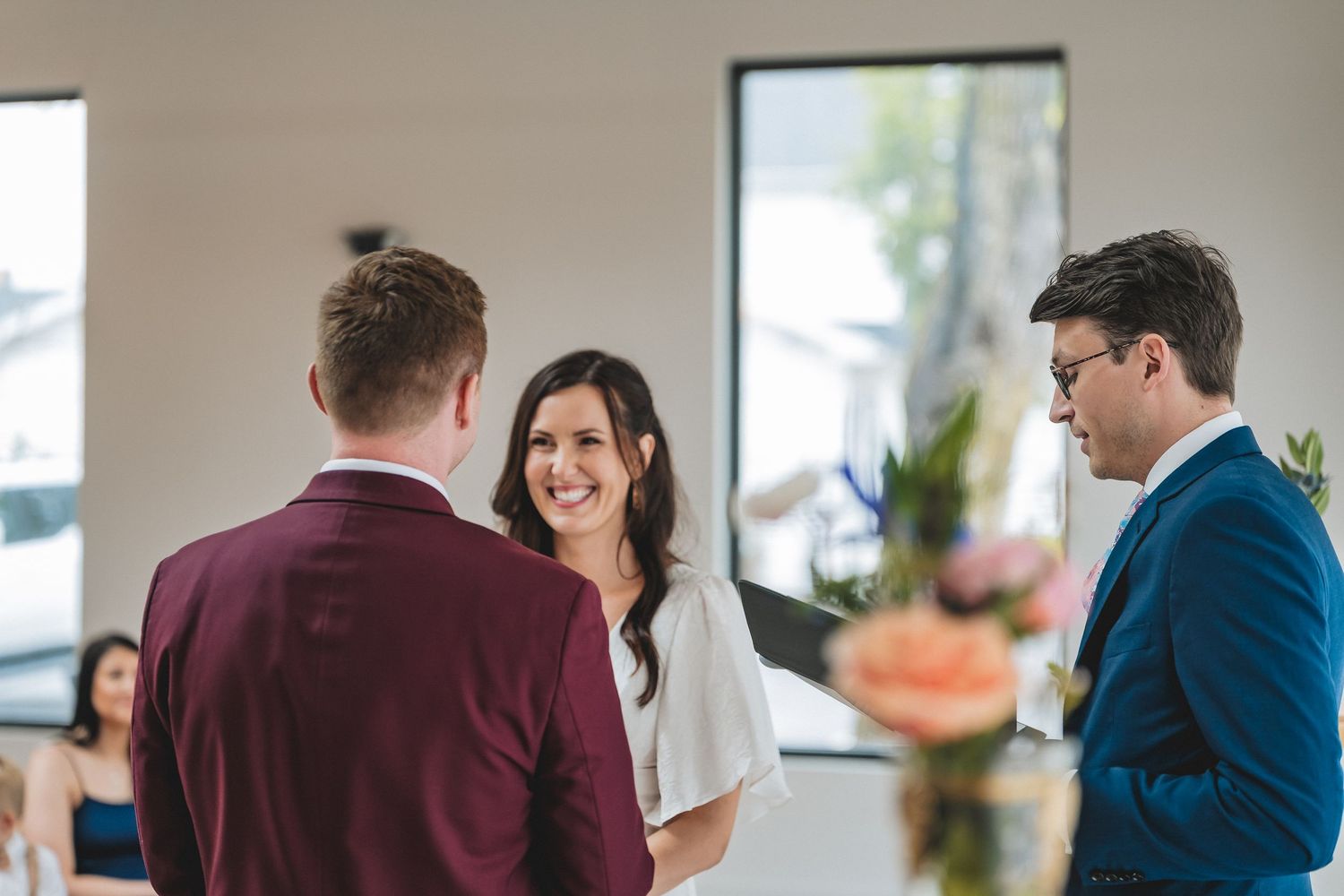 A group of people conversing during a casual indoor event with natural lighting and flowers in the background.