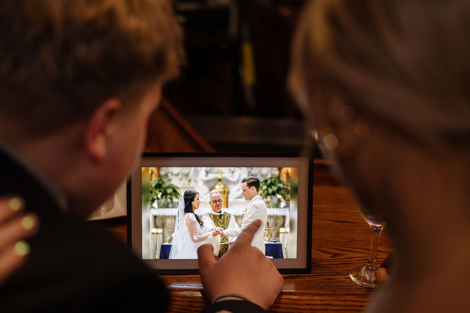 Two people view wedding photos on a tablet device at a wooden table.