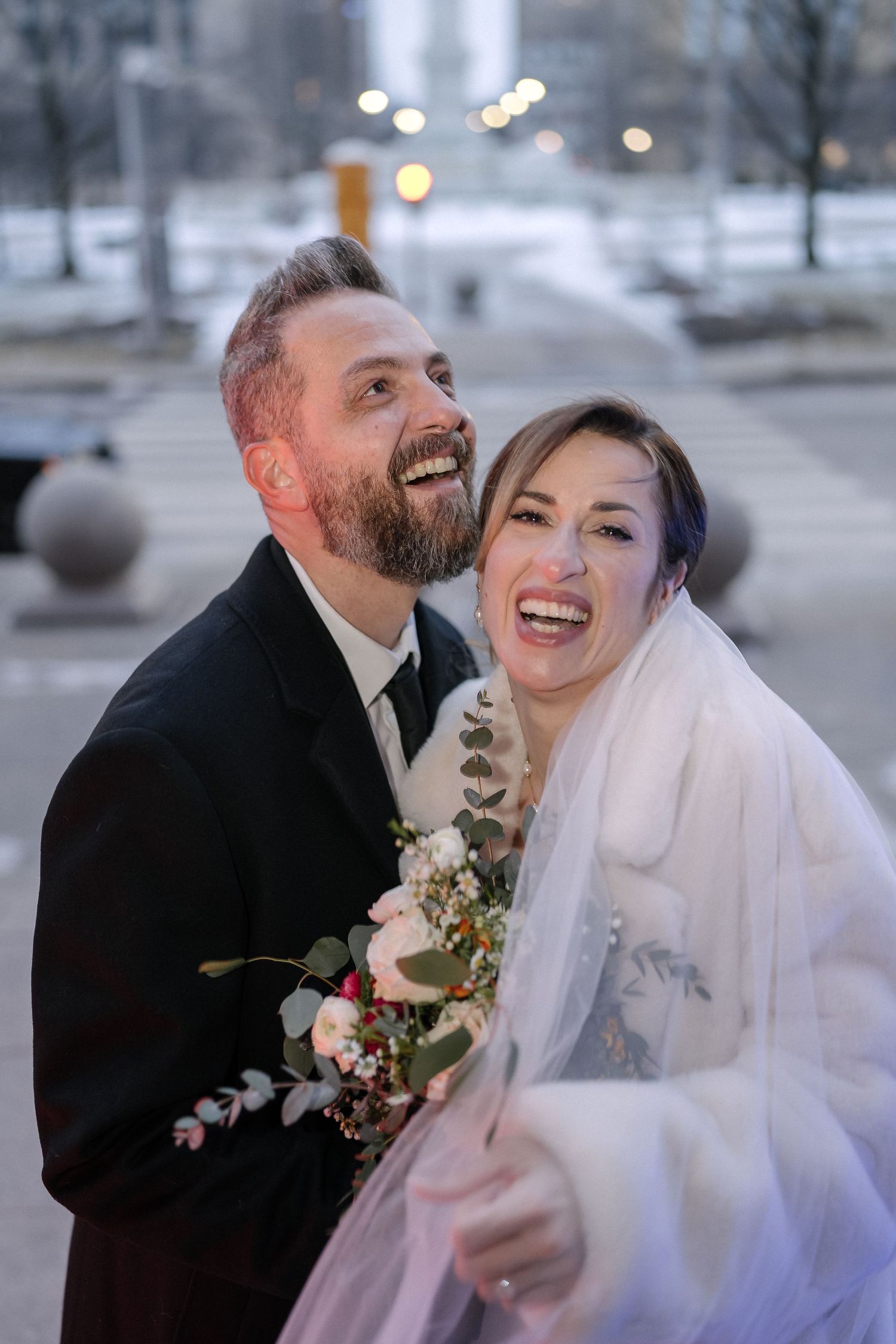 A joyful couple shares a candid laughing moment on their snowy winter wedding day. Buffalo City Hall