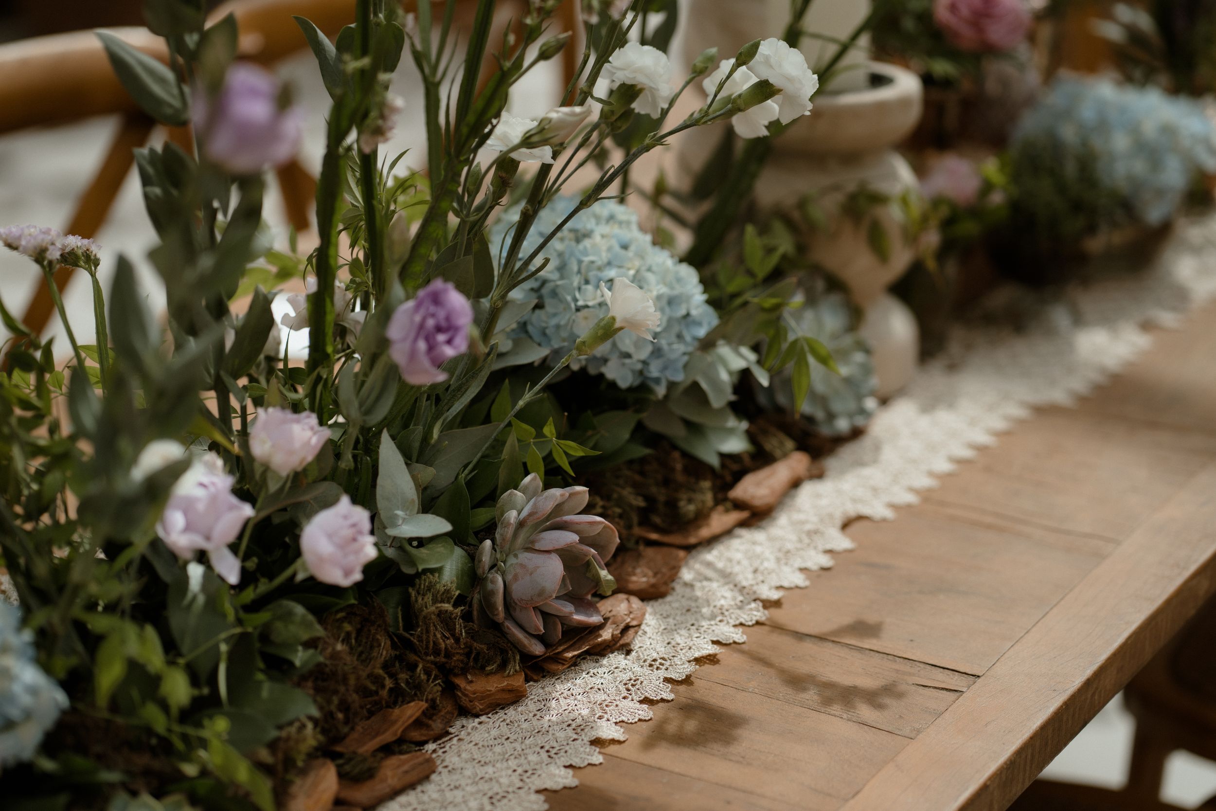 Detailed view of wedding table decorations featuring blue hydrangeas and pink flowers with lace runner.