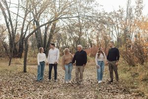 A family of six walking together on a leaf-covered path surrounded by autumn trees.