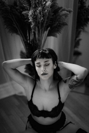 Black and white portrait of woman in black lace bralette with hands behind head, eyes closed, serene expression.