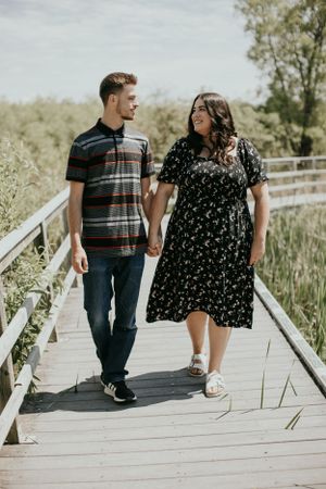Happy couple holding hands walking on wooden bridge boardwalk in casual summer outfits.