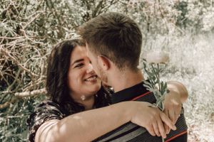 A joyful couple embraces and smiles while surrounded by lush green trees outdoors.
