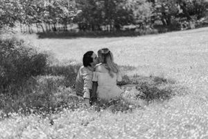 Black and white photo of couple sitting together in wildflower meadow.