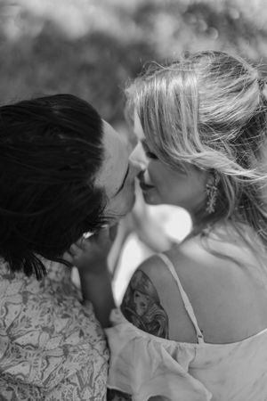 Black and white romantic closeup of couple almost kissing, woman with shoulder tattoo and earrings.