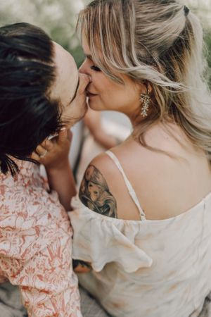 Couple sharing a romantic kiss closeup, woman with tattoo and floral earrings in white off-shoulder dress.