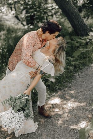 Couple sharing a dip kiss on garden path, bride holding white hydrangea bouquet in boho wedding dress.