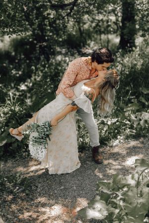 Groom dipping bride for kiss on garden path surrounded by lush greenery.